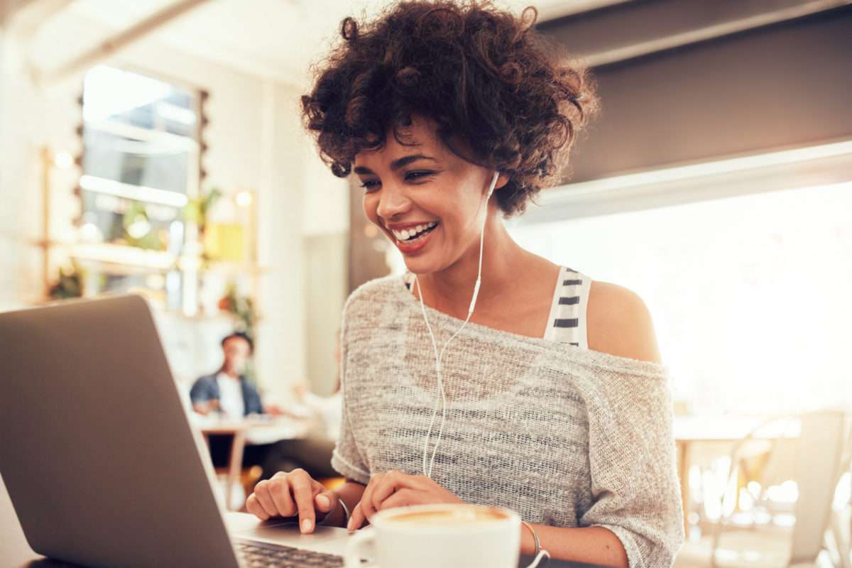 Une femme rit dans un café en train de participer à une réunion en visio conférence
