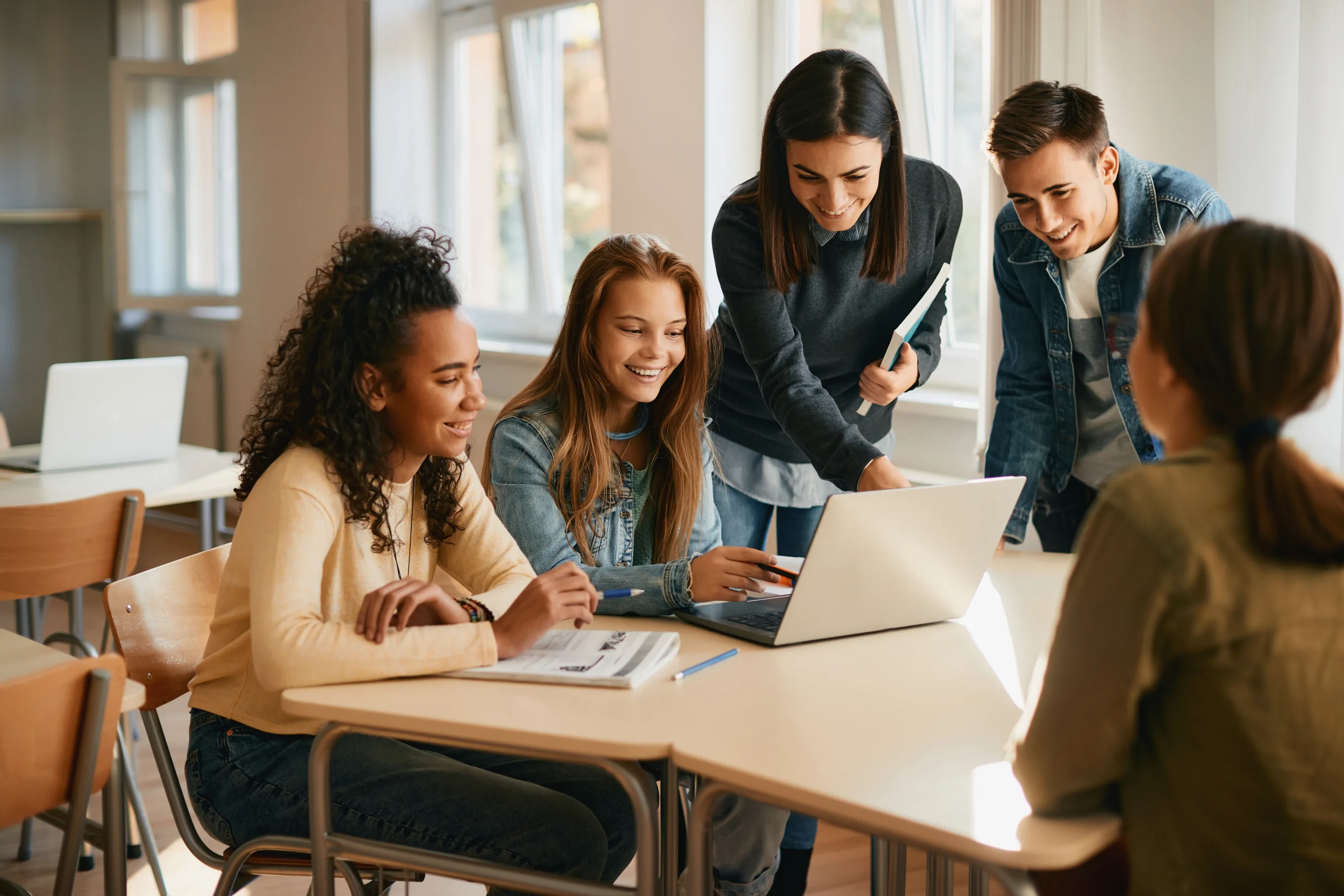 Des élèves heureux utilisant un ordinateur portable avec leur professeur d'informatique pendant un cours au lycée