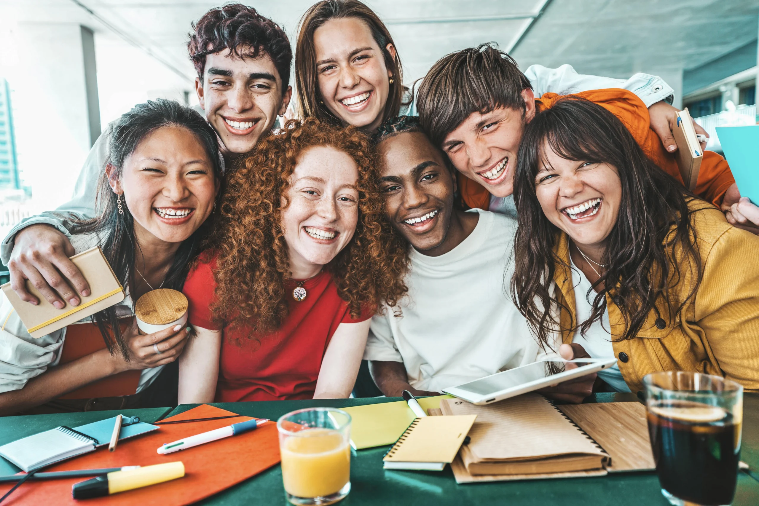 Étudiants universitaires multiraciaux assis ensemble à table avec des livres et un ordinateur portable